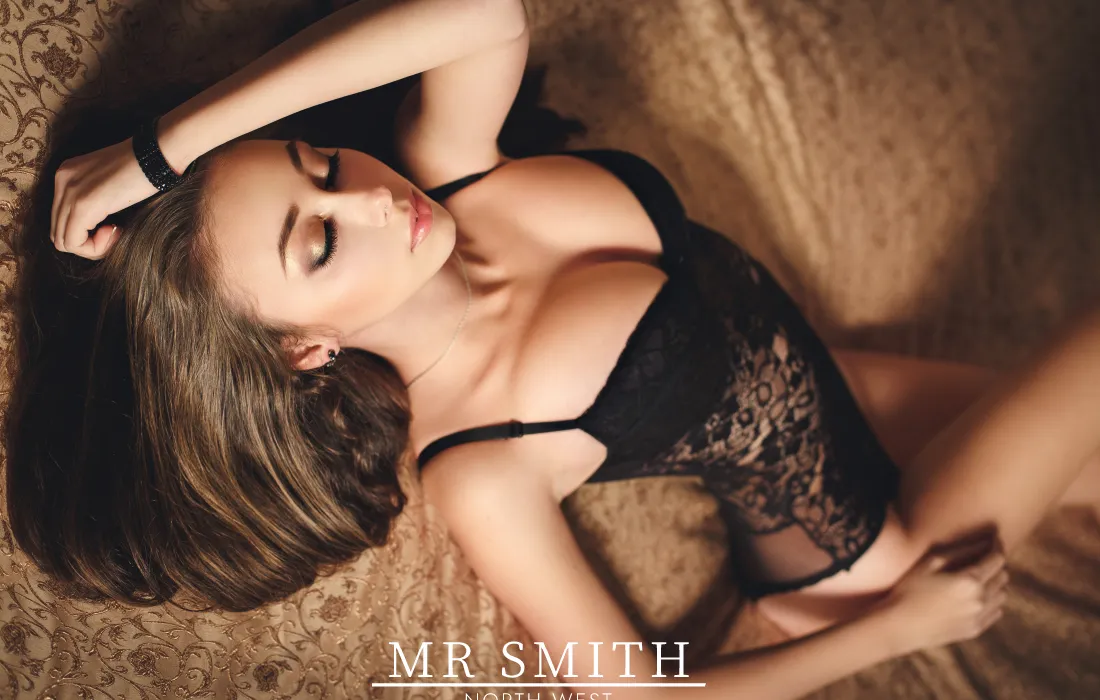 An escort lay on a bed in black lingerie